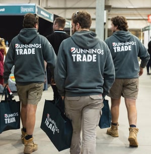 Three tradies walking through a trade expo wearing Bunnings Trade hoodies