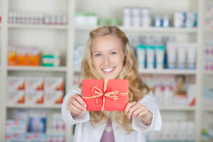 Female pharmacist holding bonus coupon card gift in pharmacy