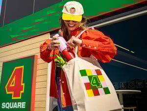 A woman walking out of a Four Square store with a branded cap, bag and drink bottle